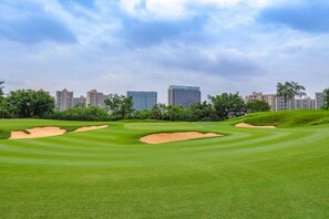 Ein Golfplatz mit Bunkern und einer Stadtkulisse im Hintergrund.