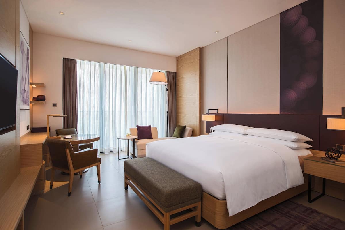 Una habitación de hotel moderna con una cama grande, un escritorio, una silla, una mesita y un televisor.