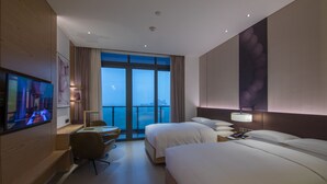 Une chambre d’hôtel avec deux lits, un bureau avec une chaise, une télévision et une grande fenêtre donnant sur la ville.