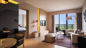 Habitación de hotel moderna con una cama grande, un escritorio, un sofá y una mesa de comedor. Cuenta con un ventanal con vistas al exterior.