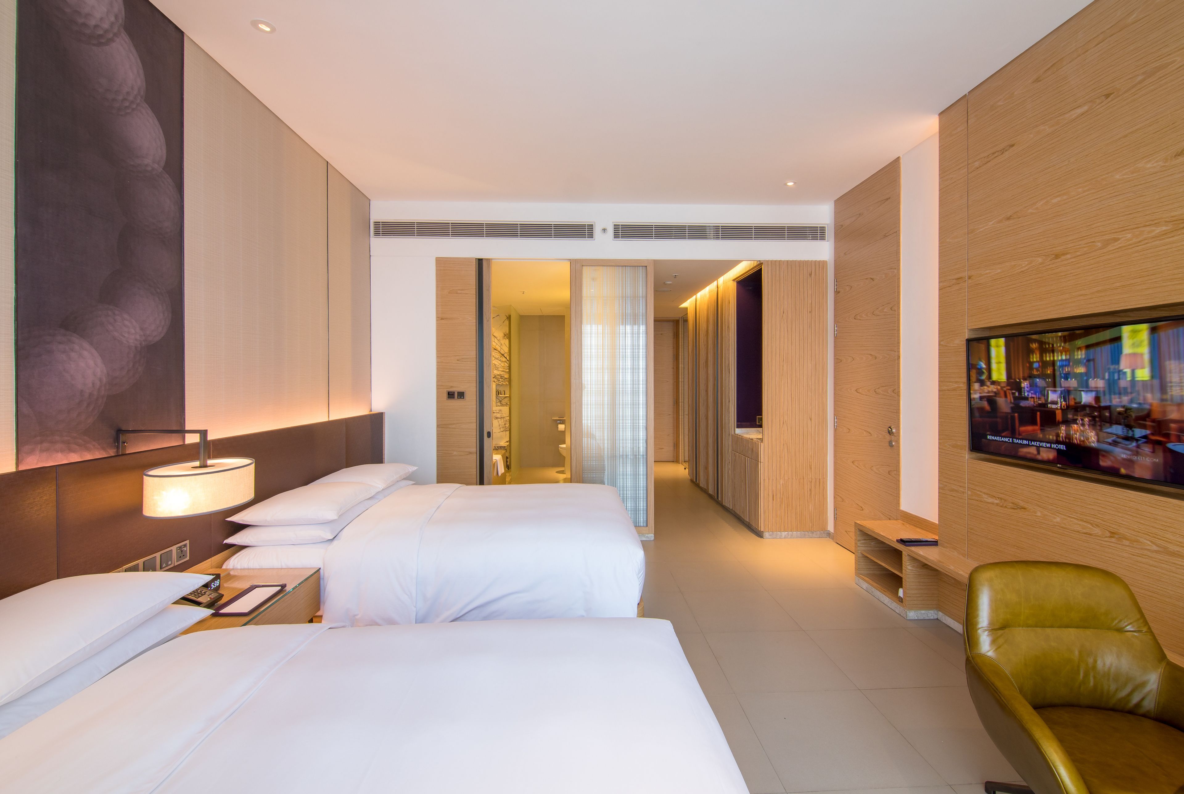 Une chambre d’hôtel avec deux lits, une télévision, un mur en bois et une salle de bain visible à travers une porte ouverte.