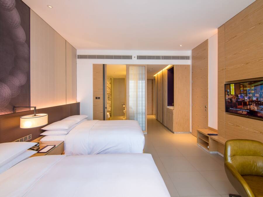 Habitación de hotel con dos camas, televisión, pared de madera y baño visible a través de una puerta abierta.