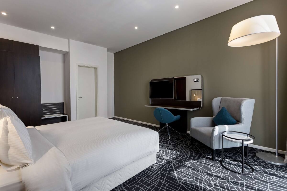 Une chambre d’hôtel comprenant un lit, un bureau avec une chaise, une télévision et une lampe de chevet.
