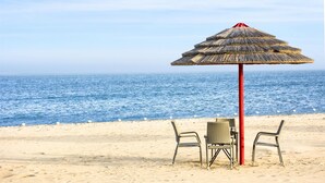 Escena de playa con una sombrilla de paja, dos sillas y una mesa.