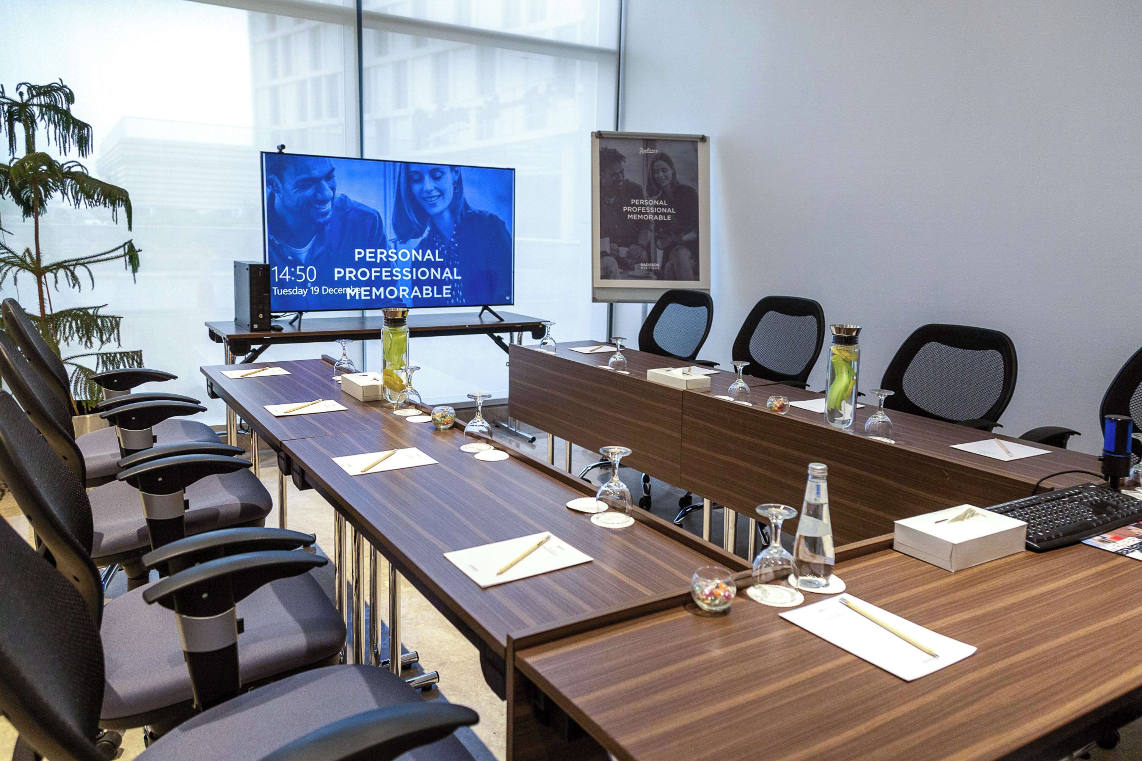A conference room with a long table, chairs, a screen displaying a video, and a poster on the wall.