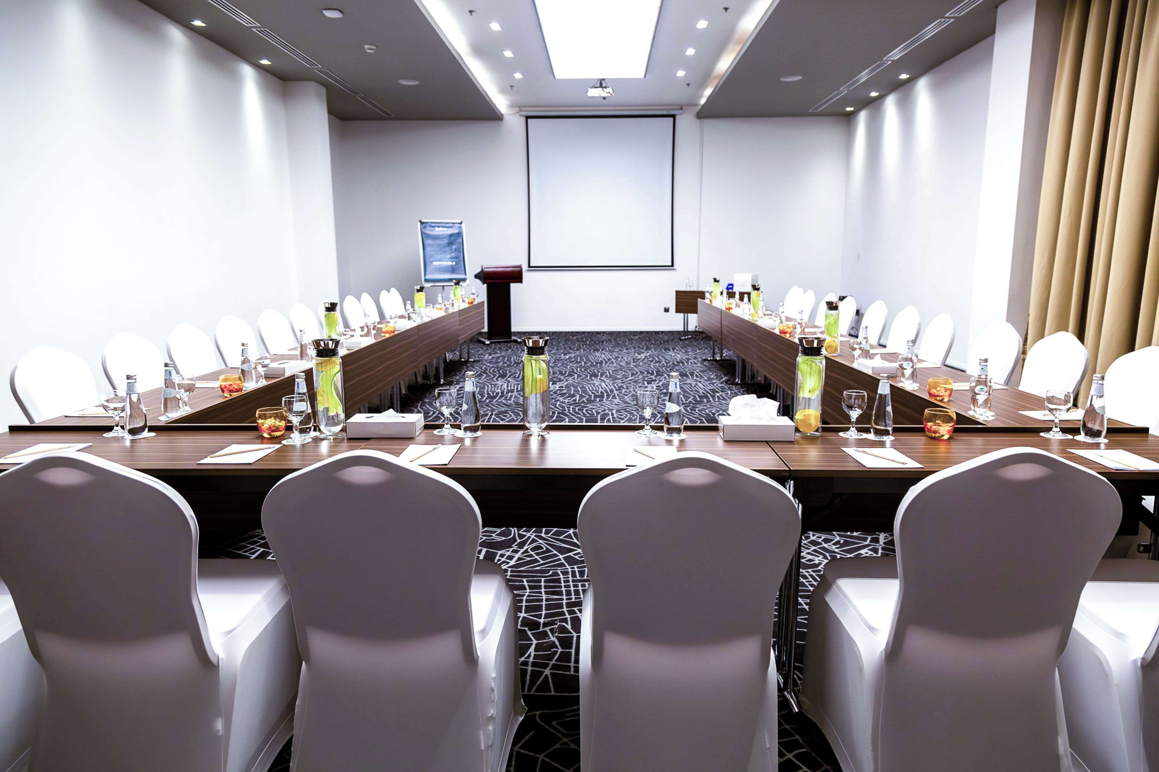 Une salle de conférence avec une longue table, des chaises blanches et un écran de projection.