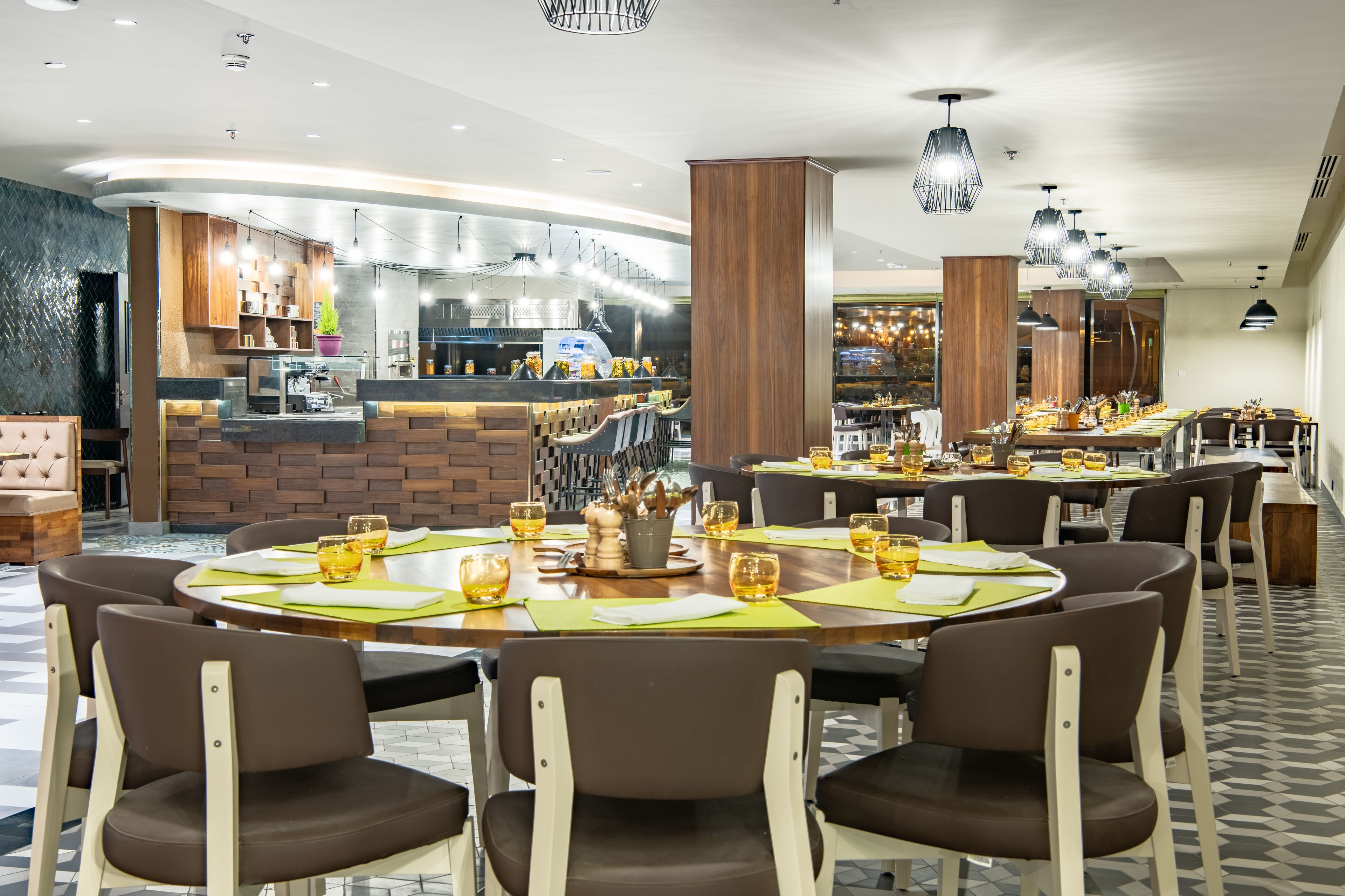 A modern restaurant with round tables, brown chairs, and a bar area with a counter and stools.