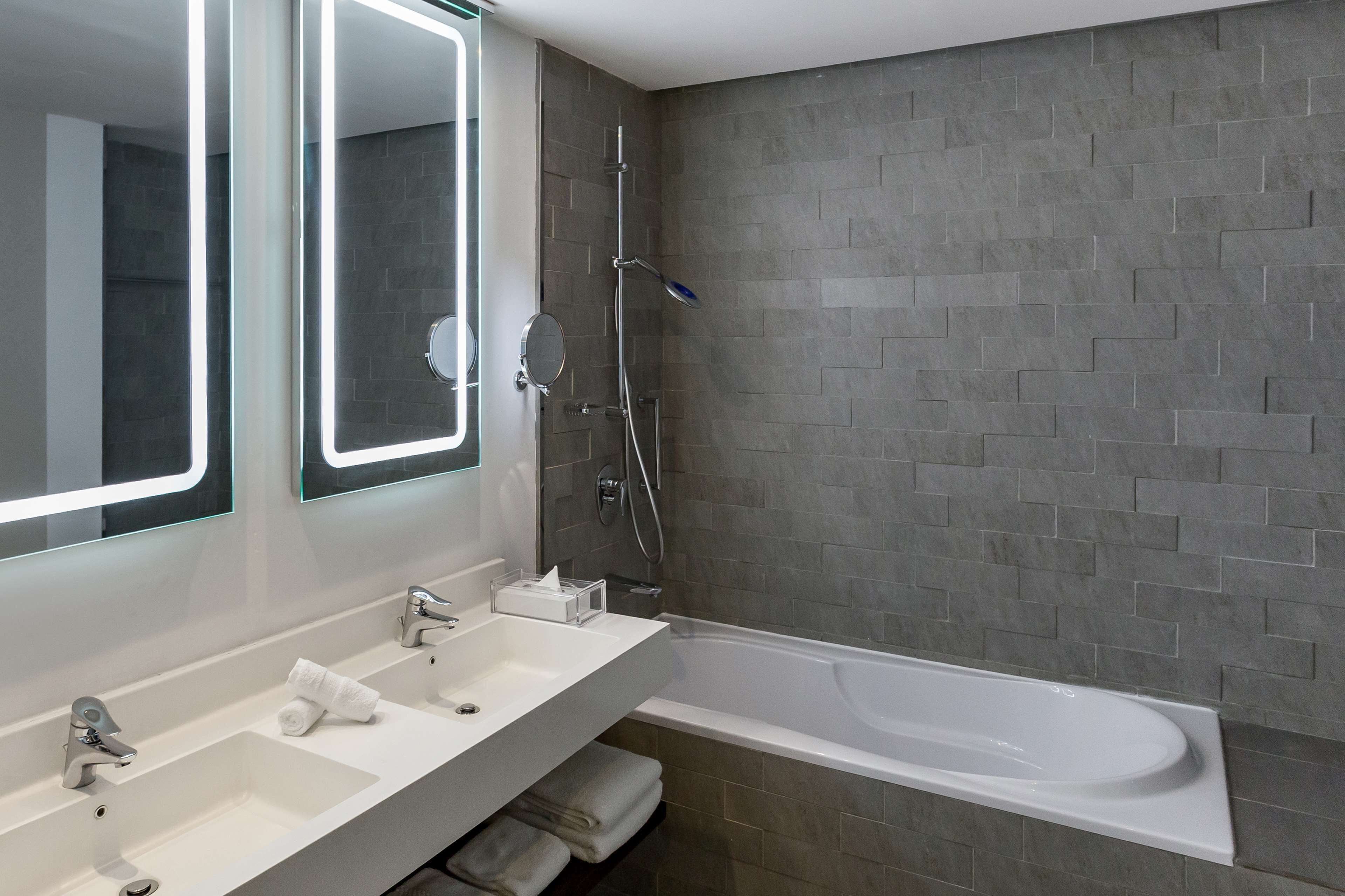 A modern bathroom with a dual sink vanity, a large mirror, a handheld showerhead, and a freestanding bathtub.