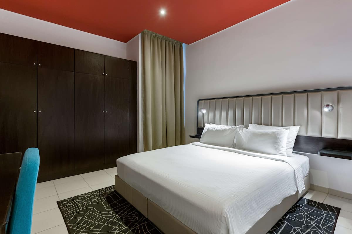 Une chambre d’hôtel moderne avec un grand lit, une armoire sombre et une grande fenêtre avec des rideaux.