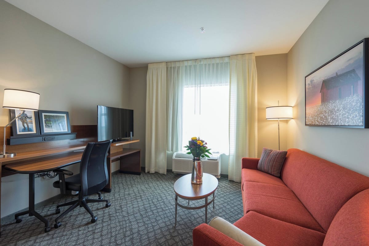A hotel room with a desk, chair, television, sofa, and a small table with a vase of flowers.