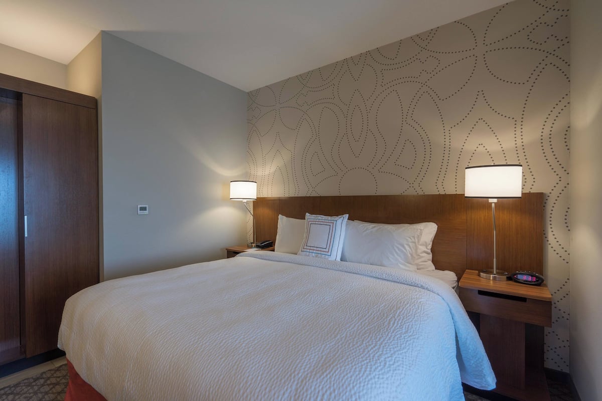 A hotel room with a large bed, two bedside tables with lamps, a wooden headboard, and a patterned wall.