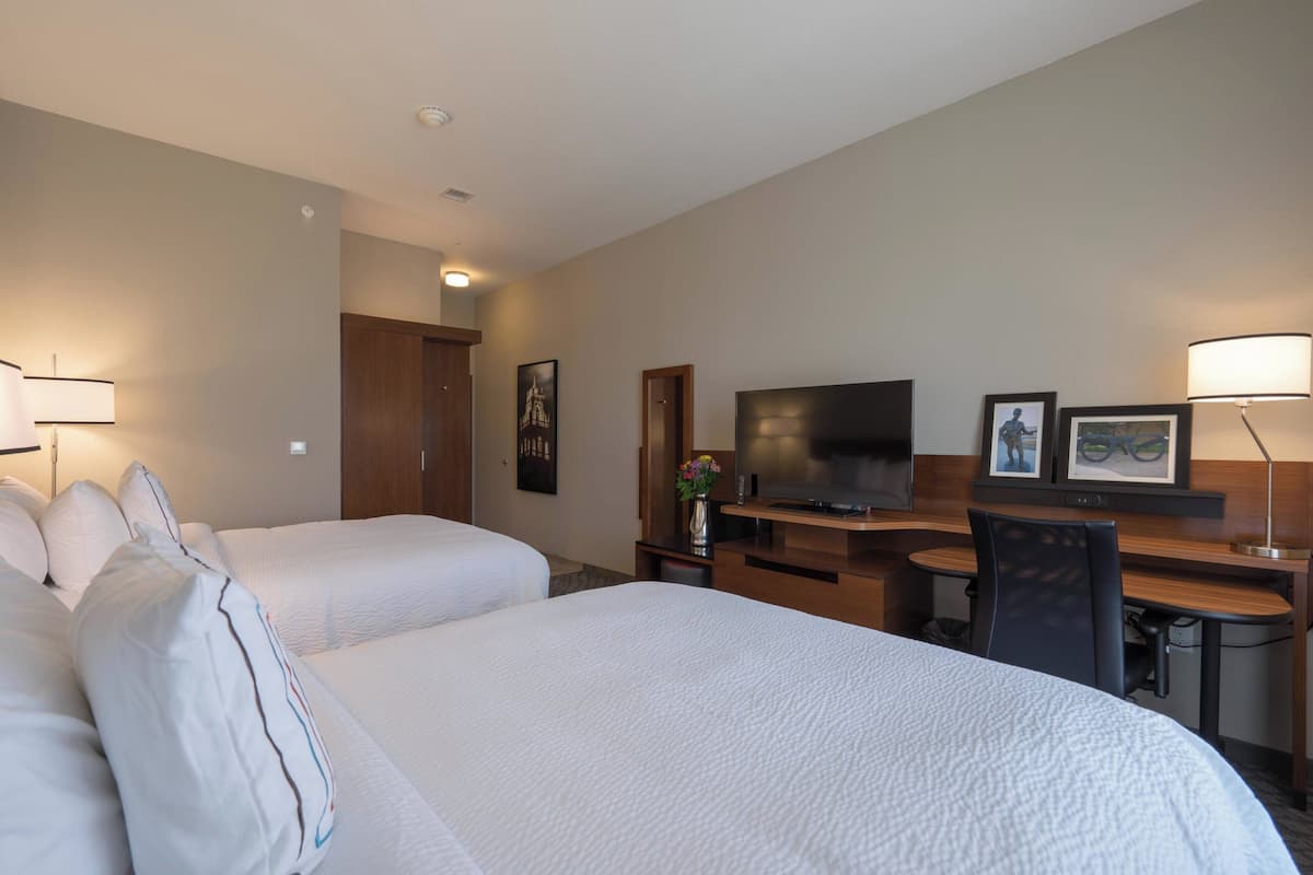 A hotel room with two beds, a desk, a TV, and a chair.