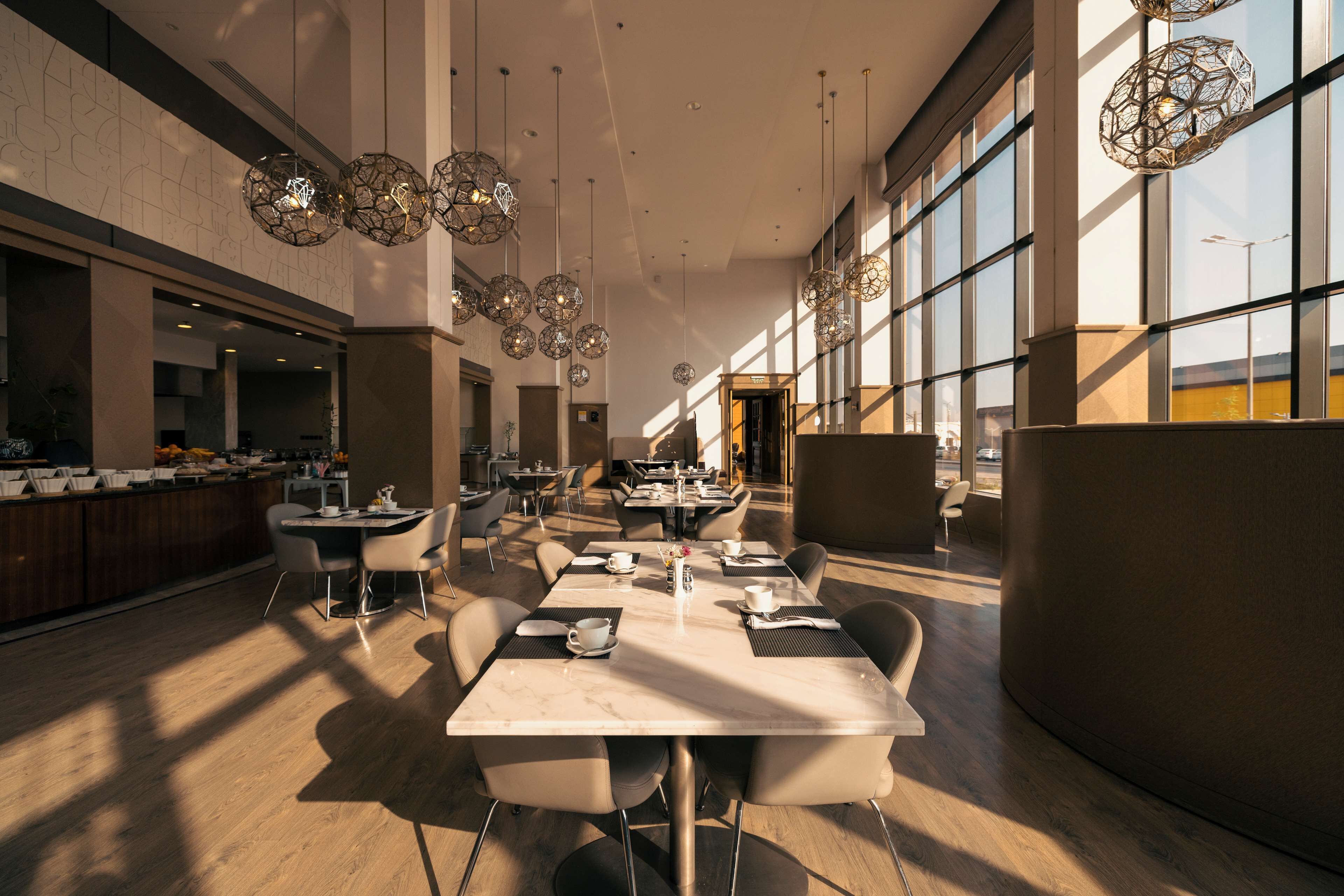 A spacious dining area with modern tables and chairs, large windows, and decorative hanging lights.