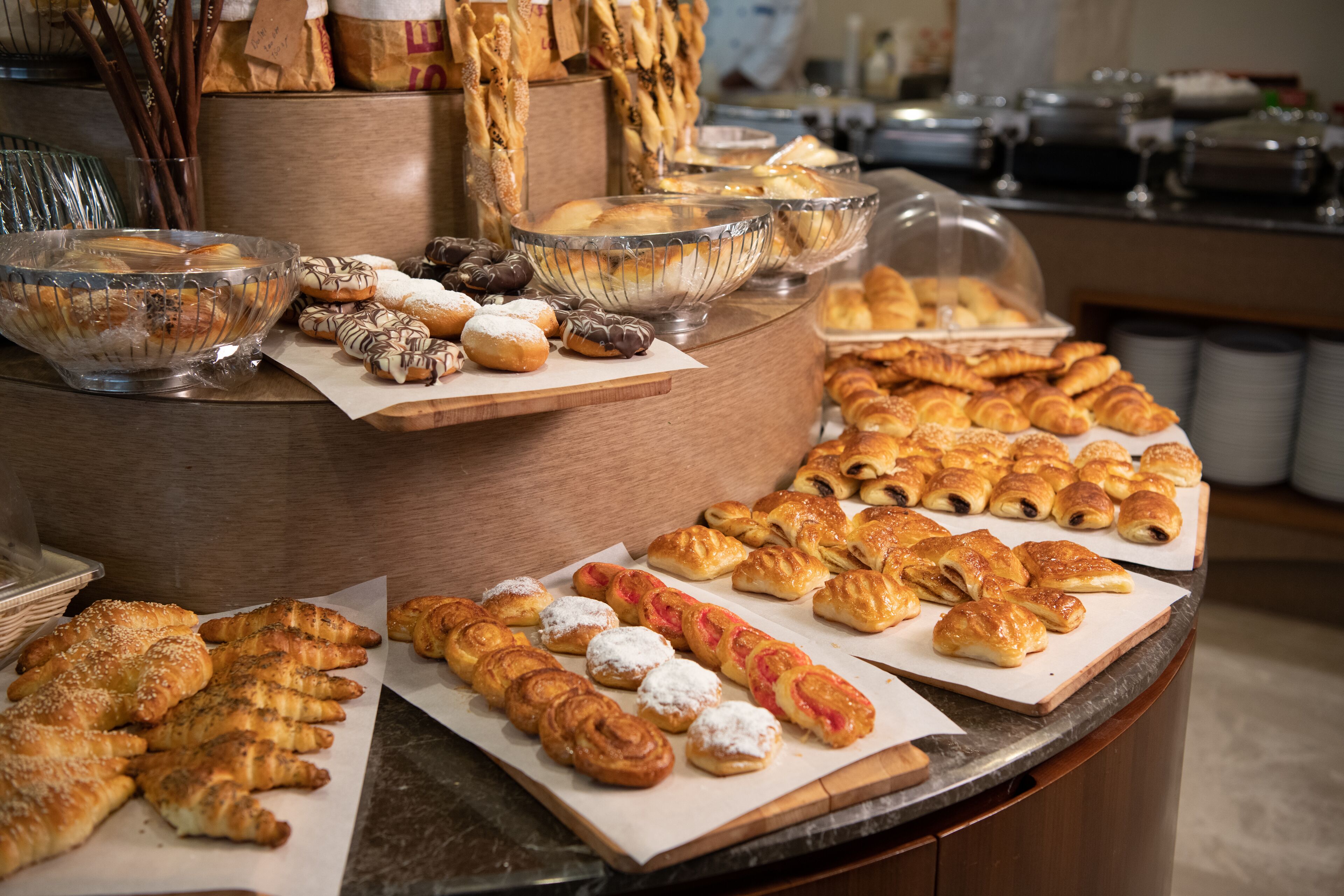 Un bufé con diversos pasteles y productos de panadería exhibidos en bandejas y tazones.