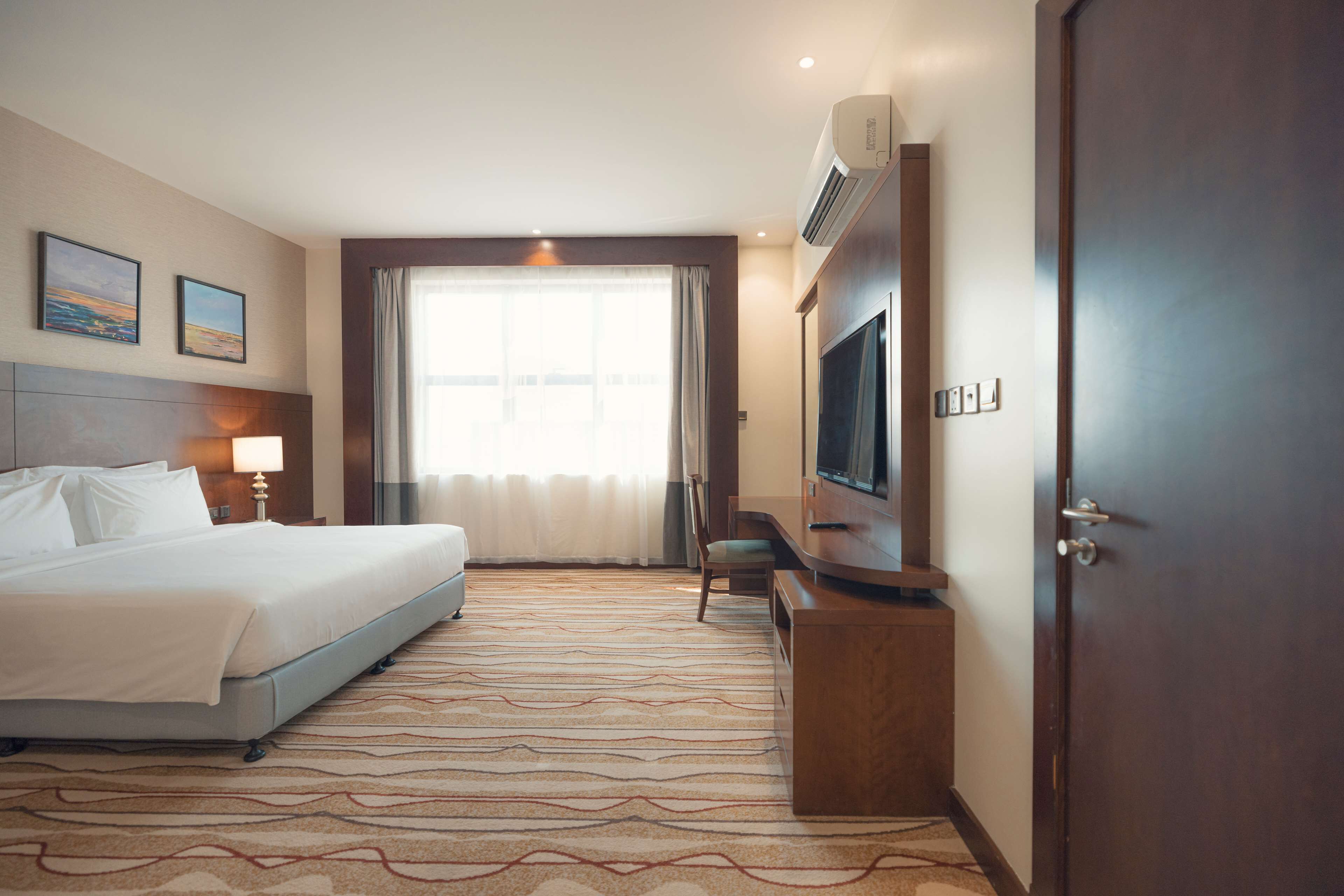 Una habitación de hotel con una cama, un escritorio, un televisor y una puerta.