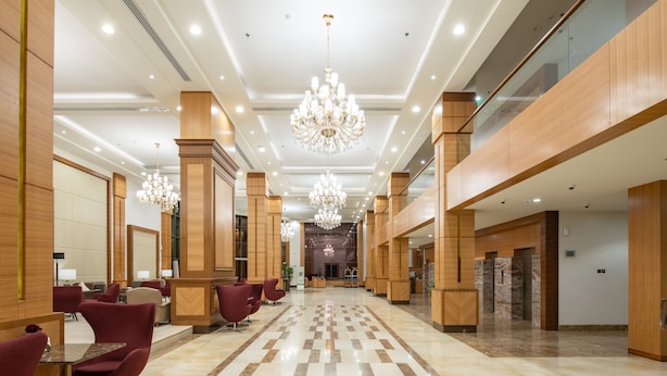 A spacious lobby with a checkered floor, wooden paneling, and red chairs. - Radisson Blu Hotel, Buraidah (Buraydah)