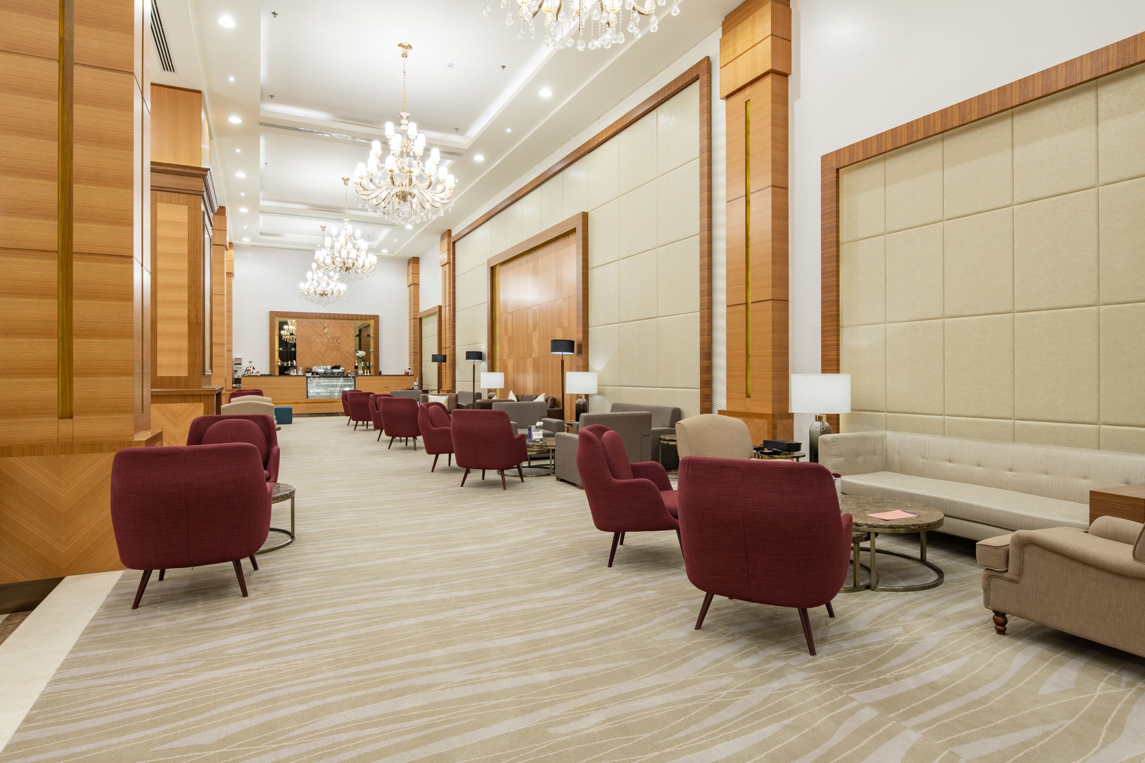 Un hall espacioso con un mostrador de recepción alargado, sillones rojos, un sofá beige y una lámpara de araña.