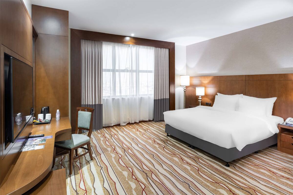 A hotel room with a large bed, a desk with a chair, a television, and a window with curtains.