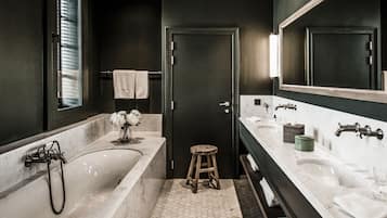 A modern bathroom with a large bathtub, two sinks, a wooden stool, and a dark door.