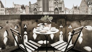 A table with chairs on a rooftop, overlooking a historic church with pointed towers. - 1898 The Post & Porter's house (Ghent)