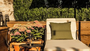 A lounge chair with a cushion, a table with a lantern, and potted plants with pink flowers.