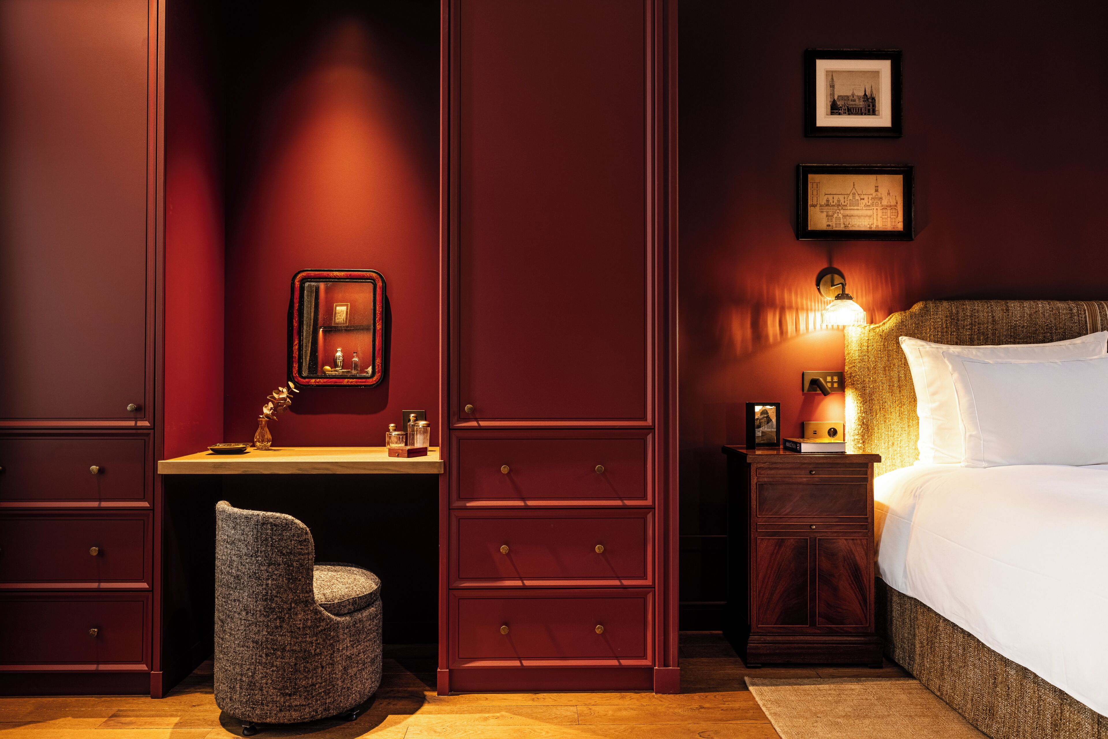 A room with a bed, a desk, a chair, and a nightstand with a lamp.