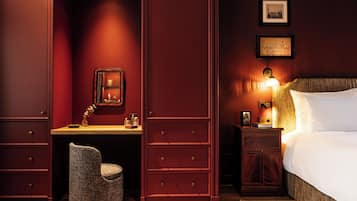 A room with a bed, a desk, a chair, and a nightstand with a lamp.