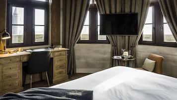 Quarto de hotel com cama, escrivaninha, cadeira, televisão e vista para um edifício pela janela.