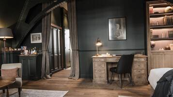 A room with a desk, chair, and bed. There is a bookshelf with books and decorative items. A lamp is on the desk.