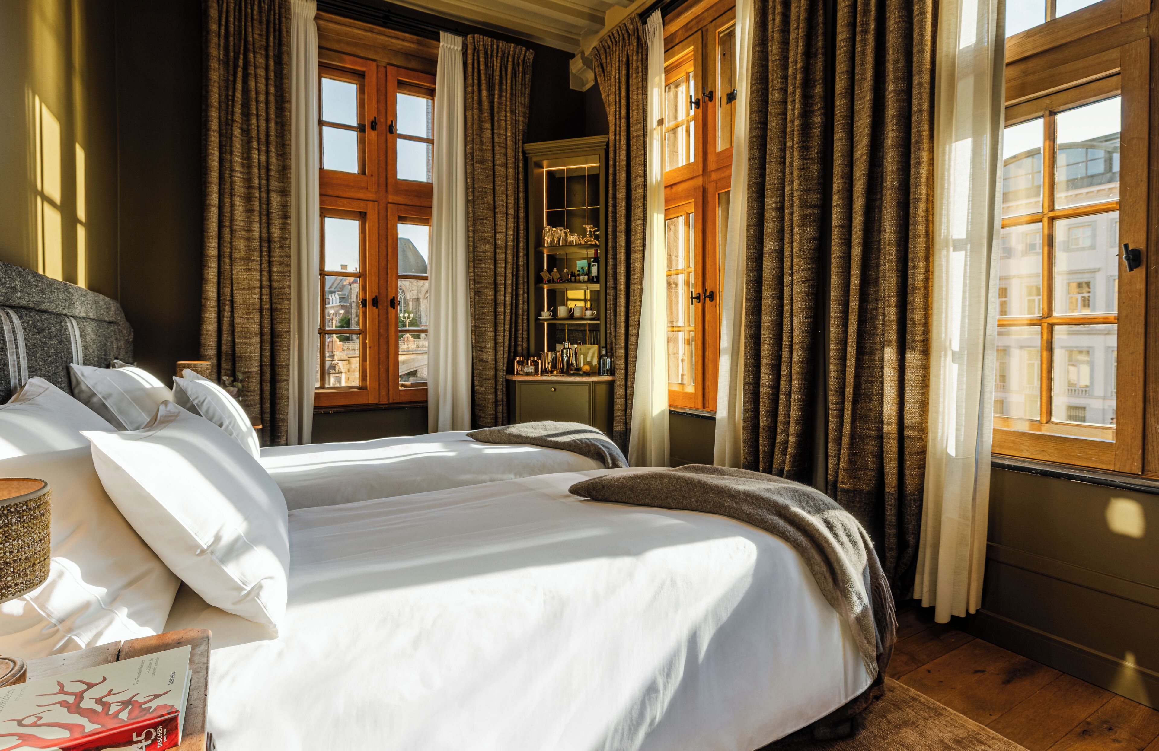 Une chambre à coucher avec un grand lit, une table de chevet, une étagère avec divers objets et une vue sur l’extérieur.