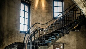 A spiral staircase with ornate metal railings and wooden handrails, leading to a landing with a wooden table and a door with a glass panel. - 1898 The Post & Porter's house (Ghent)