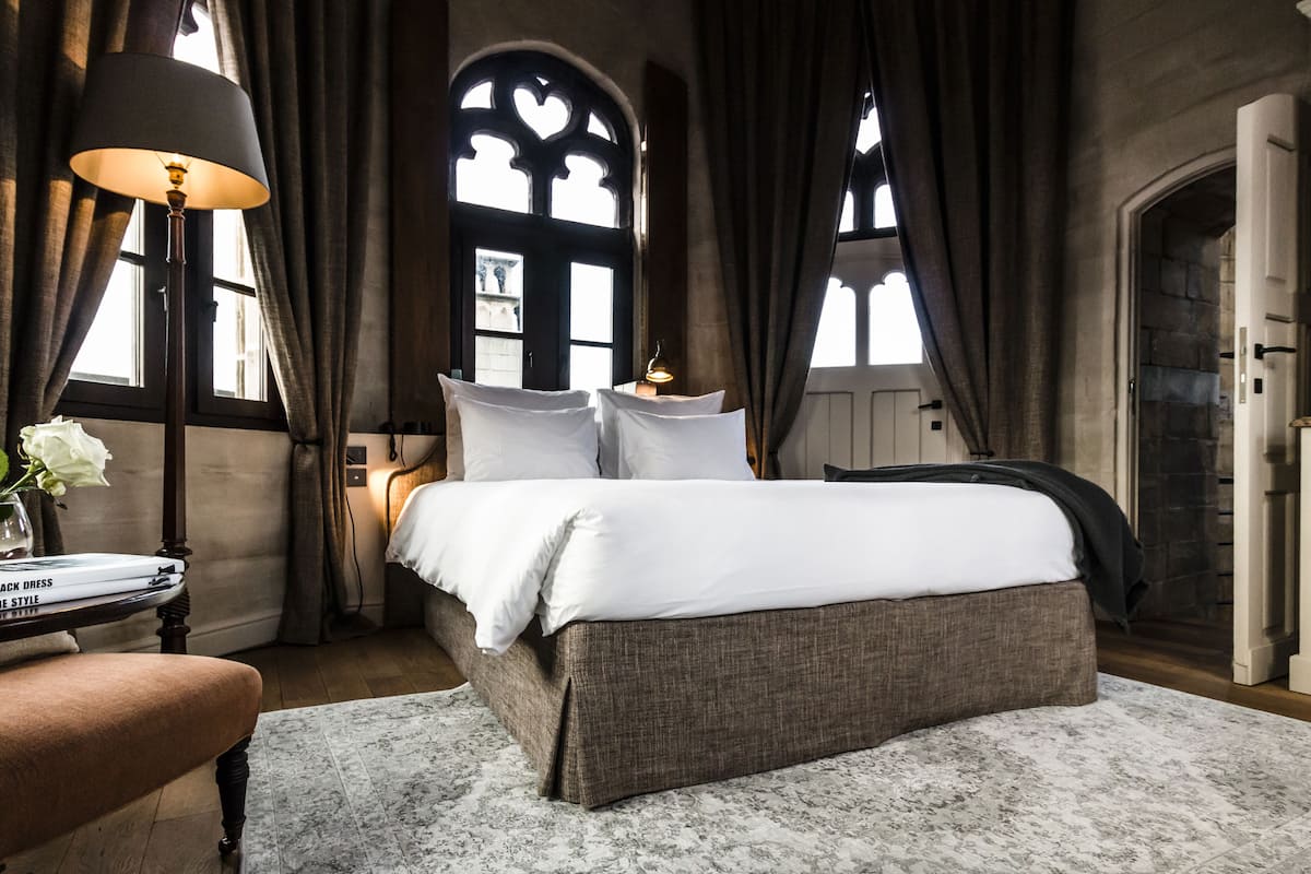 A bedroom with a large bed, a bedside table with a lamp, and a chair.