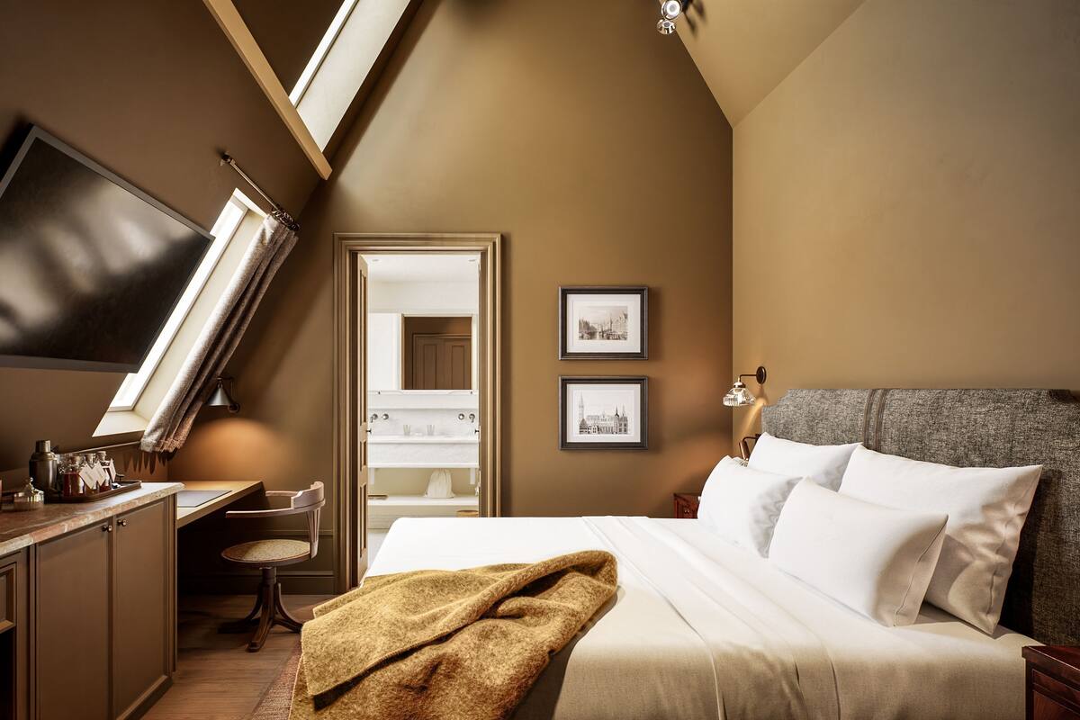 A bedroom with a bed, a desk, a chair, a TV, and framed pictures on the wall.
