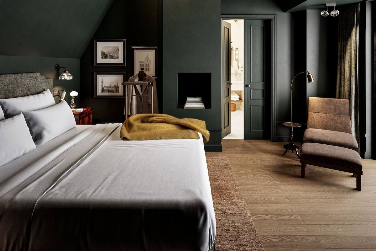 A bedroom with a bed, a chair, a desk, and a door leading to another room.