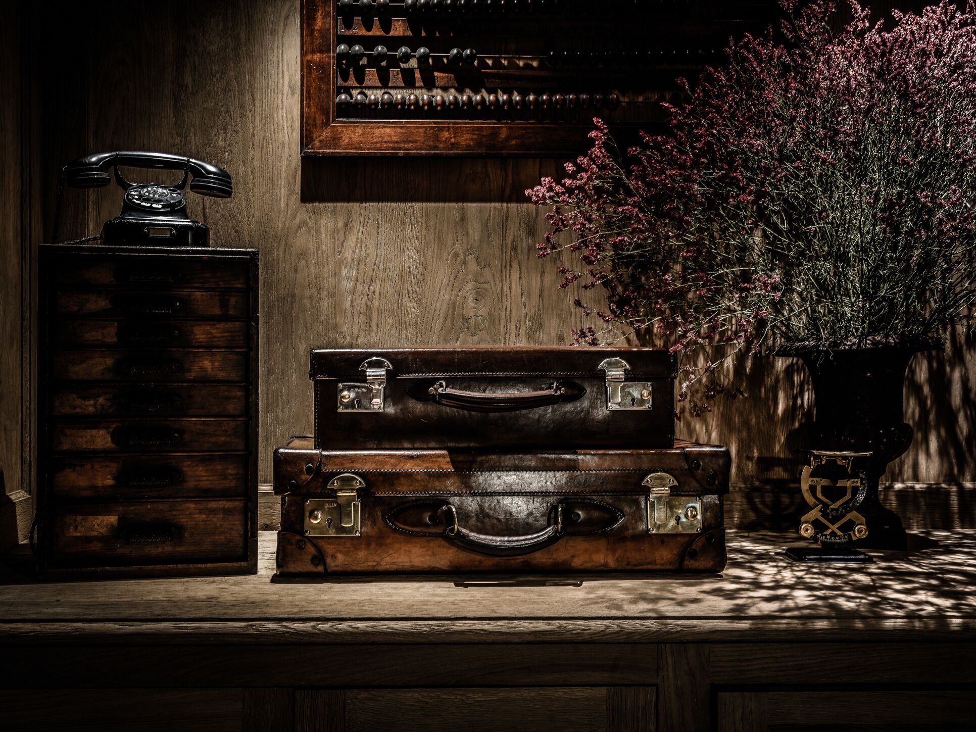 A wooden desk with vintage suitcases, a rotary phone, and a vase with flowers.