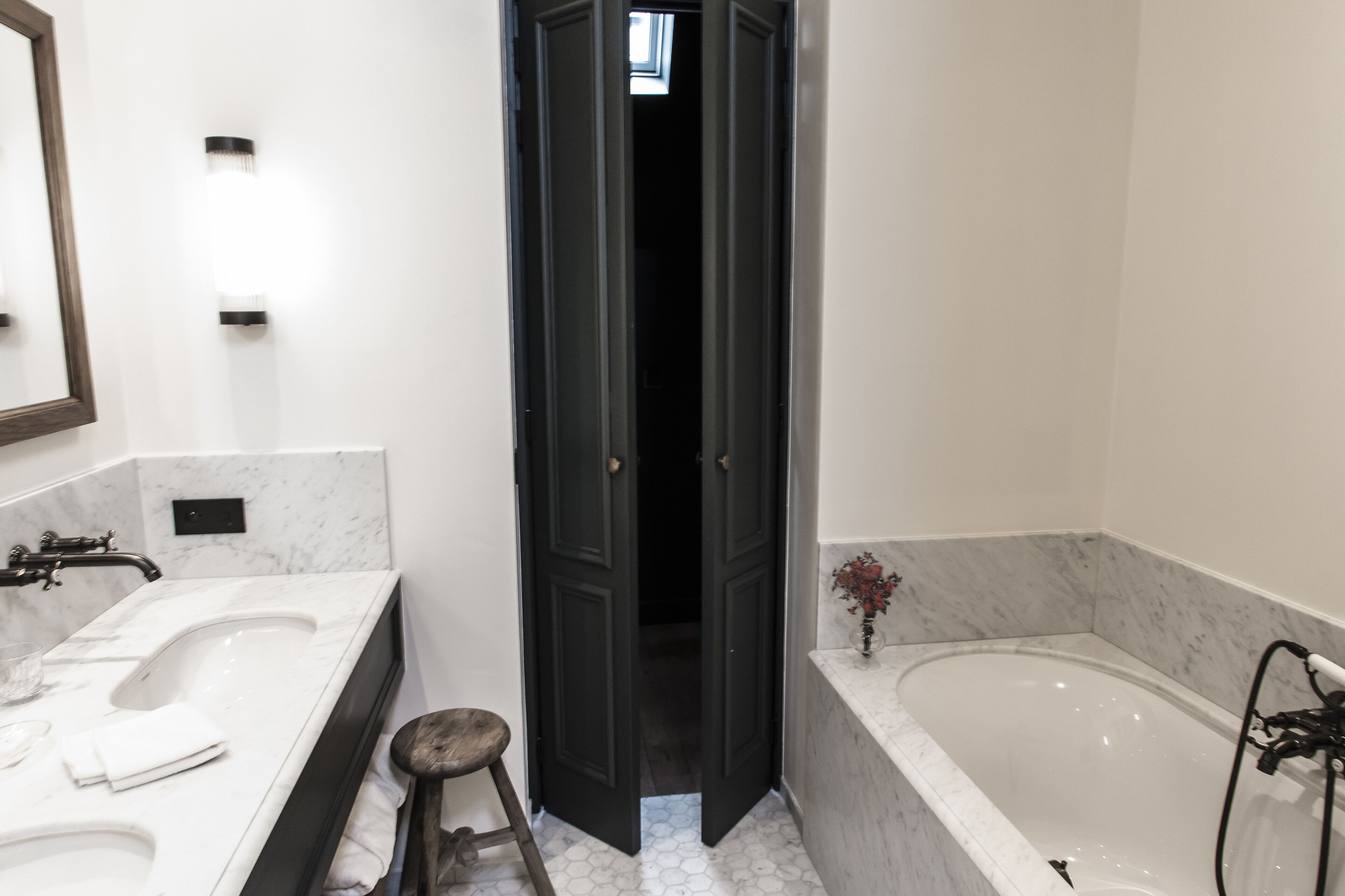 A bathroom with two sinks, a bathtub, and a dark door leading to another room.