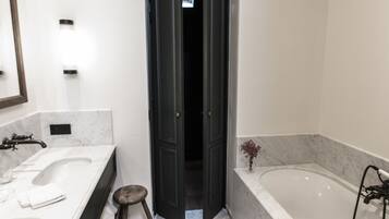 A bathroom with two sinks, a bathtub, and a dark door leading to another room.
