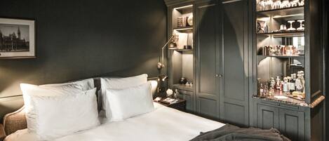Una cama bien hecha con ropa blanca, un armario de madera oscura con puertas de vidrio y un cuadro en la pared.