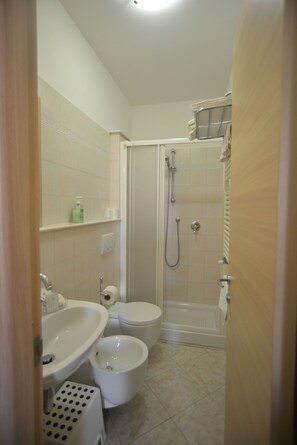 A small bathroom with a sink, toilet, bidet, and shower.
