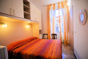 A bedroom with a bed, a chair, a small table, and a window with curtains.