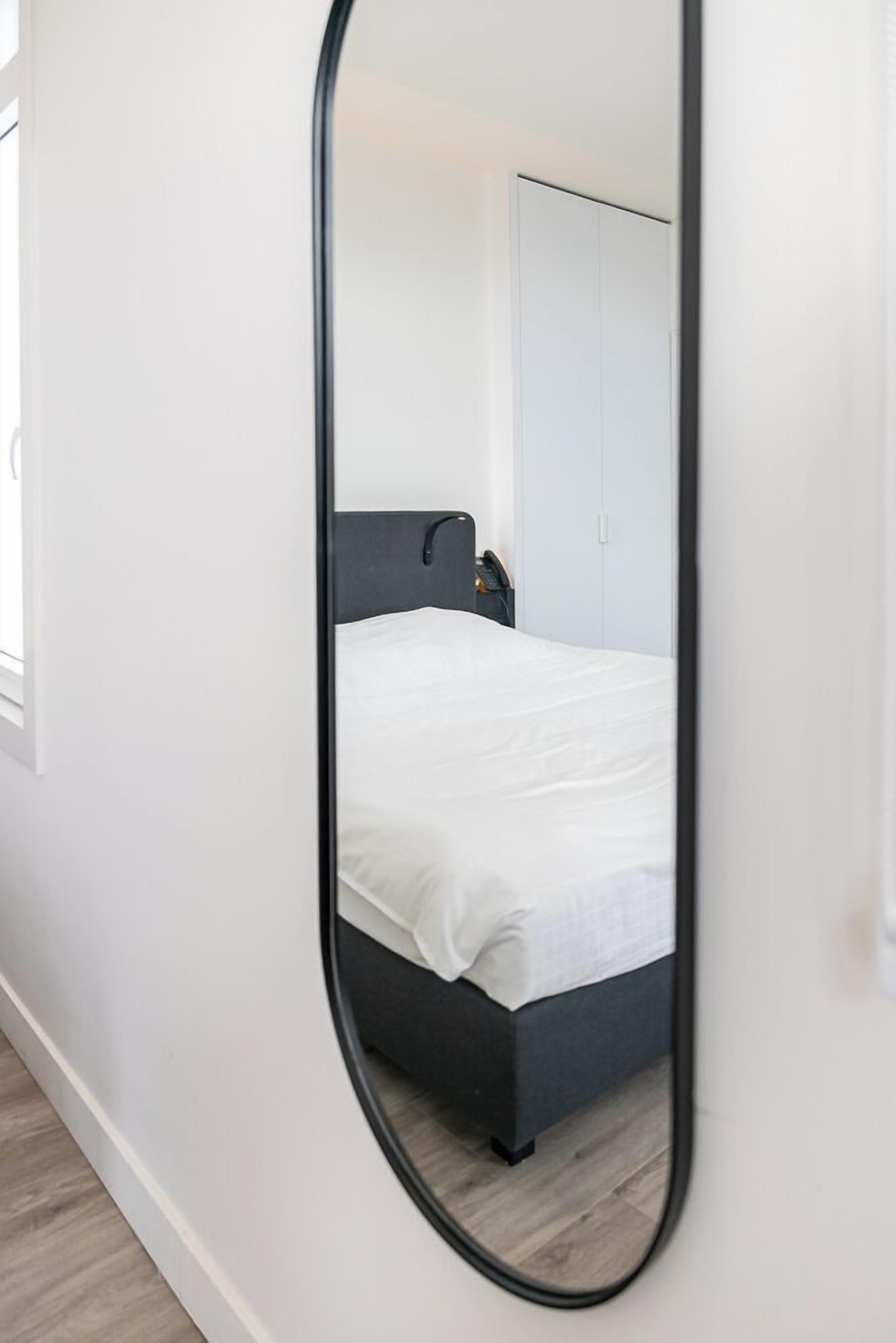 Une chambre à coucher avec un lit, une armoire et un miroir qui reflète la pièce.