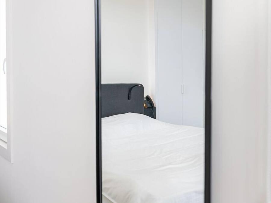 Une chambre à coucher avec un lit, une armoire et un miroir qui reflète la pièce.