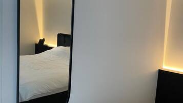 Un dormitorio con un espejo grande, una cama, una mesita de noche y una mesilla.