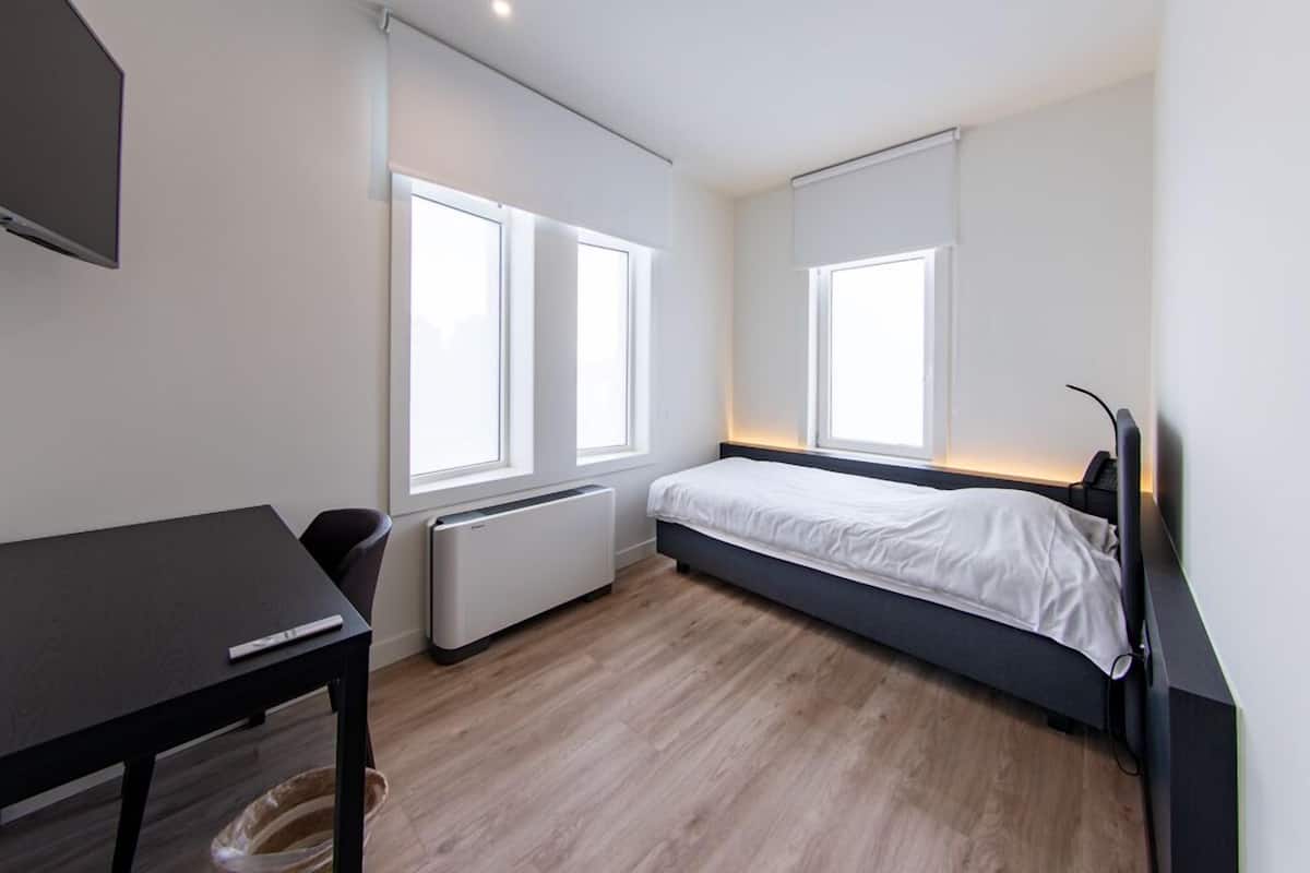 A modern bedroom with a bed, a desk, and two windows.