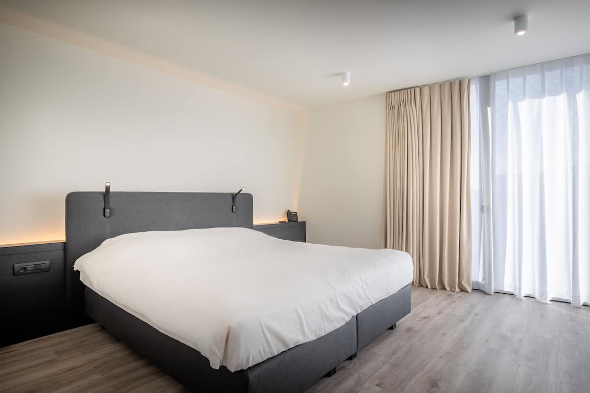 A modern bedroom with a large bed, bedside tables, and a large window with curtains.