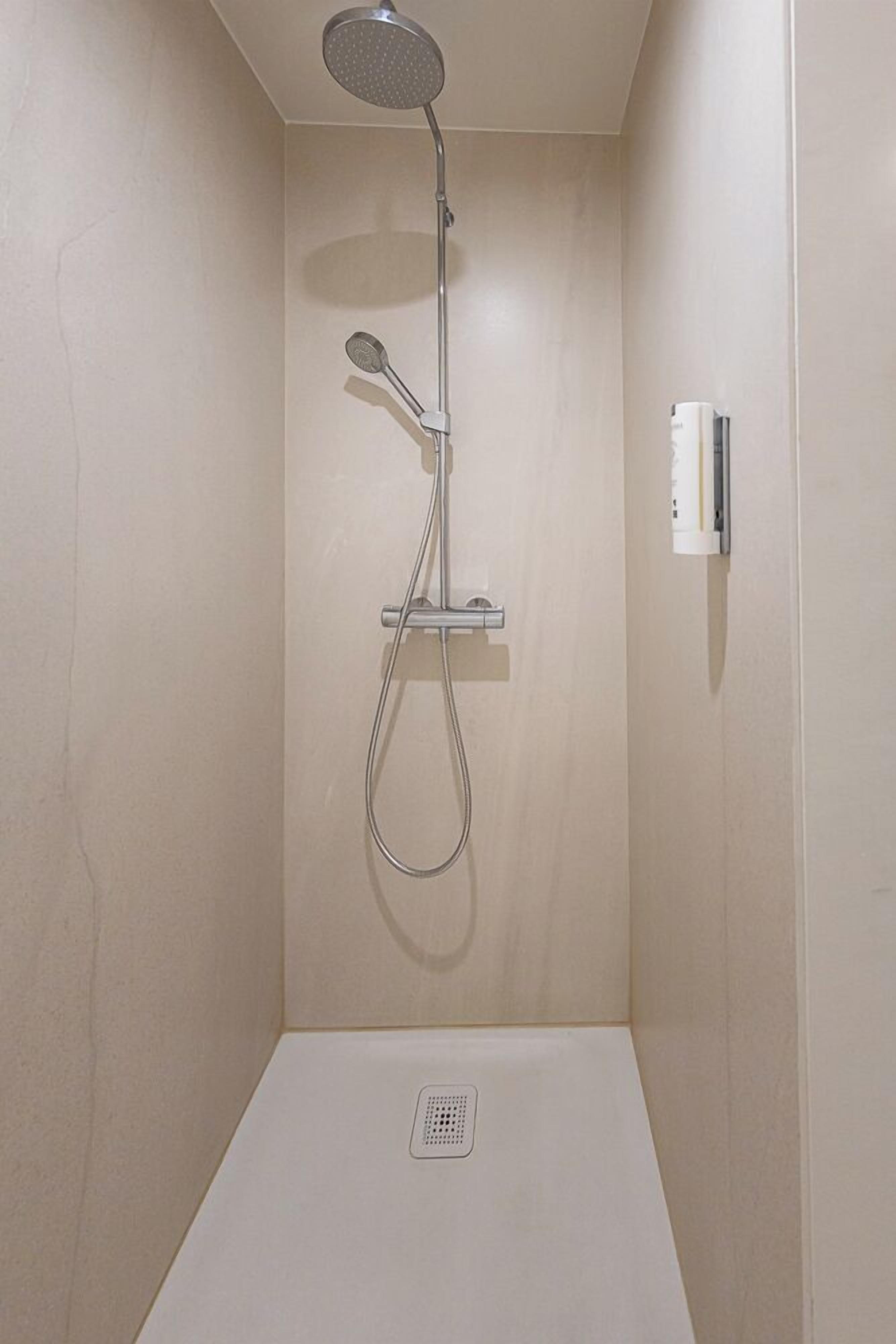 A small, enclosed shower area with a handheld showerhead and a wall-mounted control panel.