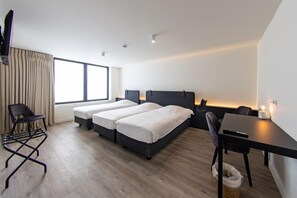 Une chambre d’hôtel moderne équipée de deux lits simples, d’un bureau, d’une chaise, d’une télévision et d’une grande fenêtre avec des rideaux.