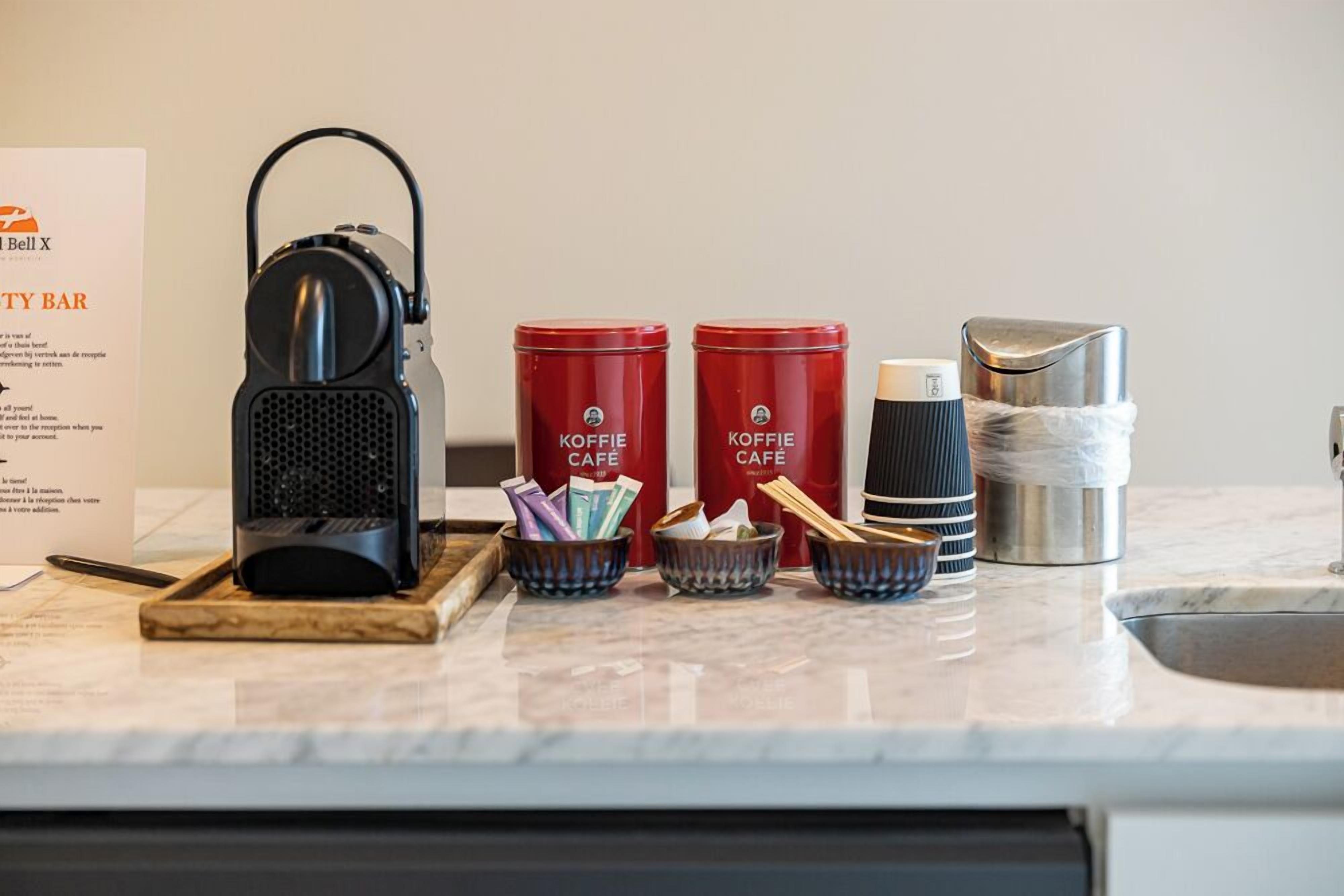 Un coin café comprenant deux récipients rouges de la marque Koffie Café, une bouilloire électrique noire et un thermos en acier inoxydable, le tout posé sur un comptoir en marbre.