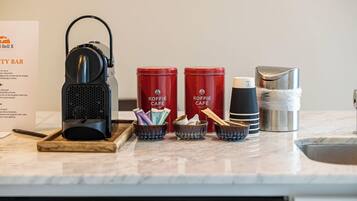 Un coin café comprenant deux récipients rouges de la marque Koffie Café, une bouilloire électrique noire et un thermos en acier inoxydable, le tout posé sur un comptoir en marbre.