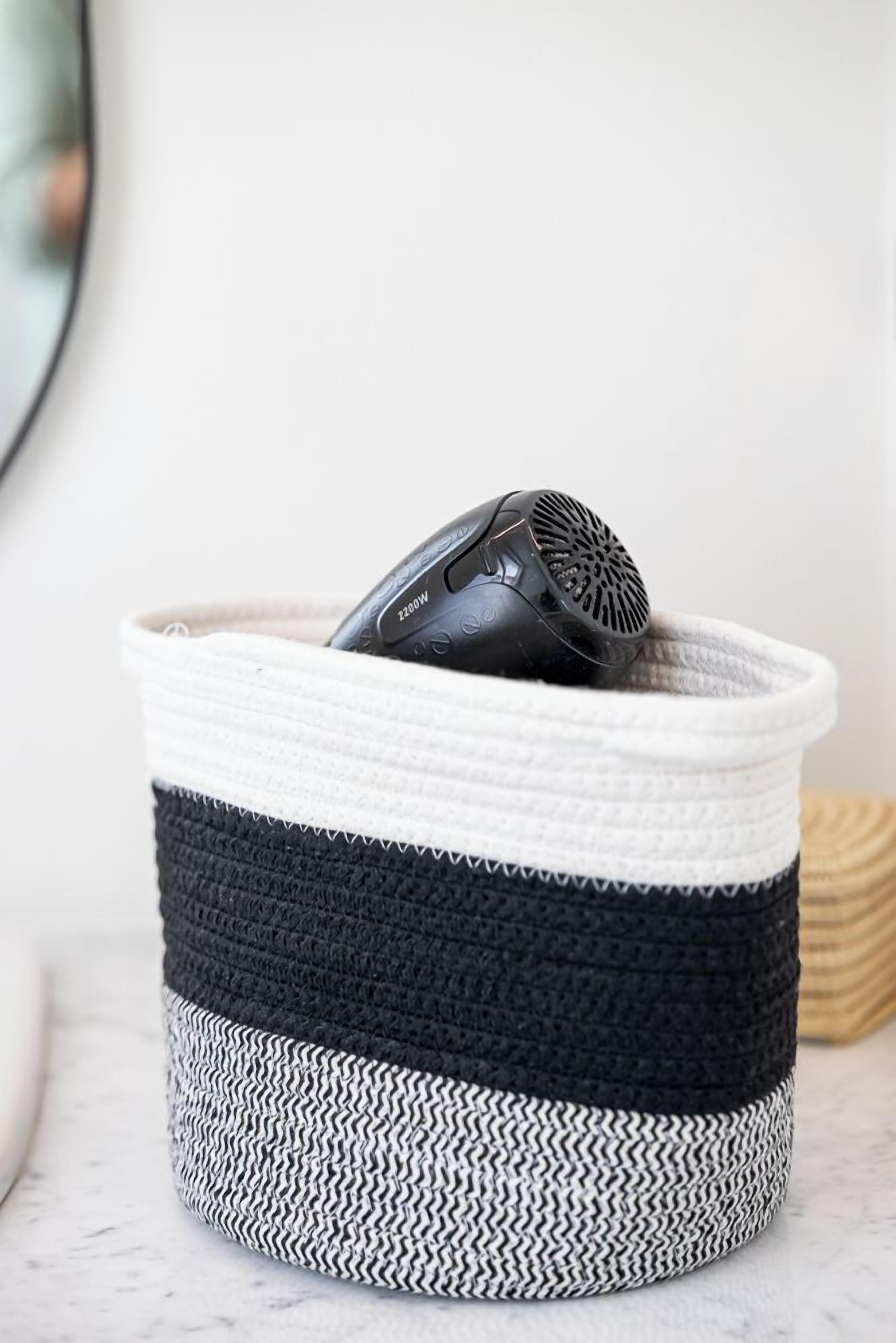Un panier tressé à motifs noirs et blancs, contenant un objet noir.